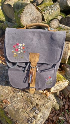 Kundenbild des grauen Daypack Acadia - Wildblüte Rucksacks, der im Freien auf einem Stapel Holzscheite ruht.