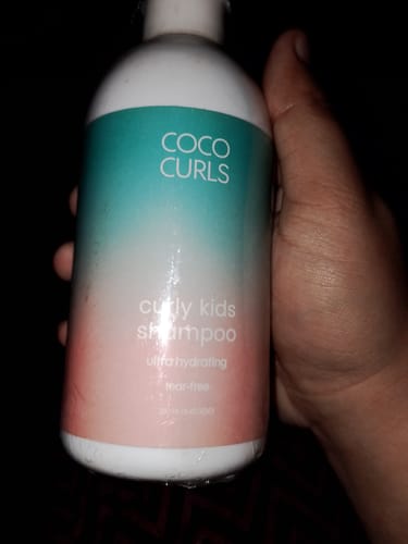 Customer's hand holding a wet bottle of Coco Curls Curly Kids Shampoo.