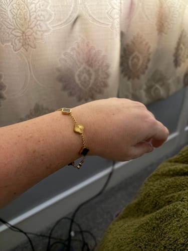 Customer wearing a gold bracelet with square charms in different colors on their wrist.