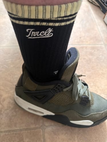 Customer wearing black SCRIPT CREW SOCKS with a striped cuff, shown with an olive green sneaker.