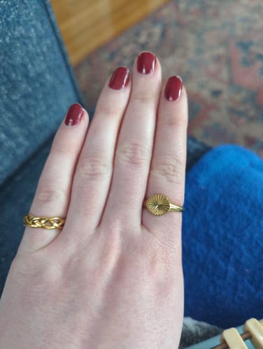 Customer's hand showing two waterproof gold rings. One ring has a braided design and the other has a sunburst signet style.
