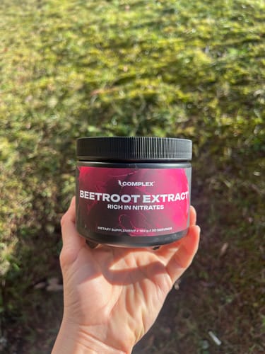 Customer holding a black tub of Beetroot Extract outdoors over a grassy area.