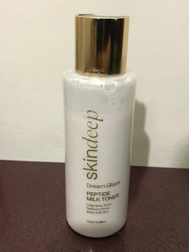 Customer's bottle of Dream Glaze Peptide Milk Toner, showing the white bottle and gold cap, sitting on a counter.