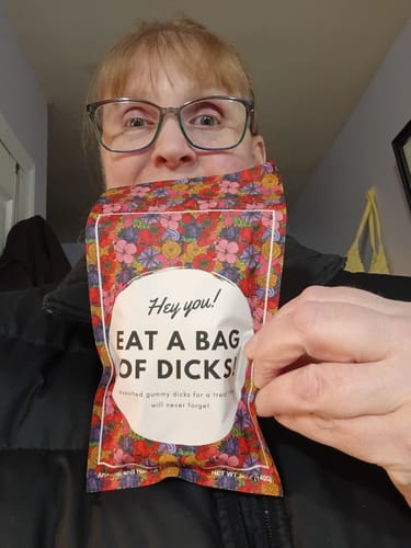 Reviewer holding up a colorful, floral-patterned bag of Gummy Candy D's with humorous text on the label.