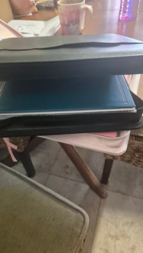 Reviewer's black Luxe Zip-up Planner Folio shown closed and full of items, sitting on another book.