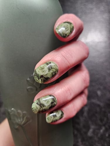 Nahaufnahme der Hand einer Kundin, die die 'Sage Rose' UV-Gel-Nagelfolien mit einem glänzenden Rosenmuster in Salbeigrün trägt.