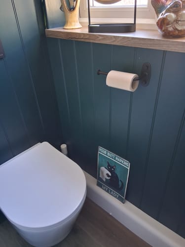 Customer's Unbleached Bamboo Toilet Paper on a holder in a bathroom with dark green paneling.