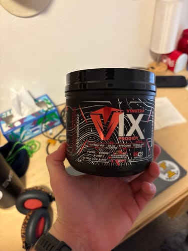 Reviewer holding a black tub of V1X PRODIGY pre-workout in their hand.