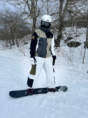 Customer on a snowboard wearing the baggy, multi-pocket color-block snow pants on a snowy slope.