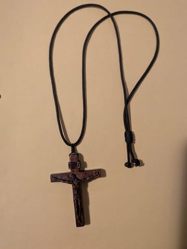Reviewer's dark wood Jesus Crucifix necklace showing its simple design and adjustable black cord.
