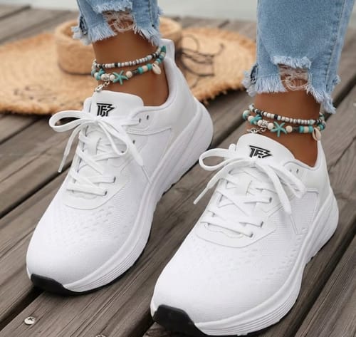 Customer wearing the white Wide Fit shoes with distressed jeans and anklets on a wooden surface.