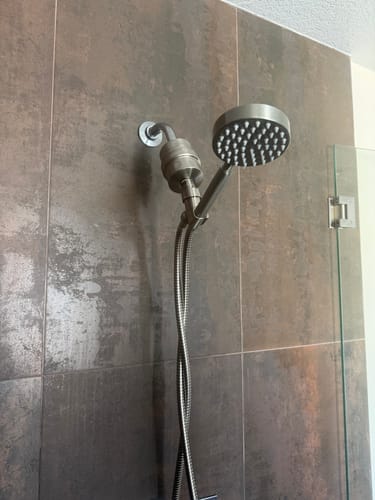 Customer's handheld shower head and filter set installed against a dark, tiled shower wall.