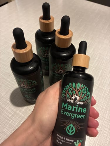 Ein Rezensent hält eine Flasche Omega 3 Algenöl in der Hand, mit drei weiteren Flaschen auf dem Tisch.