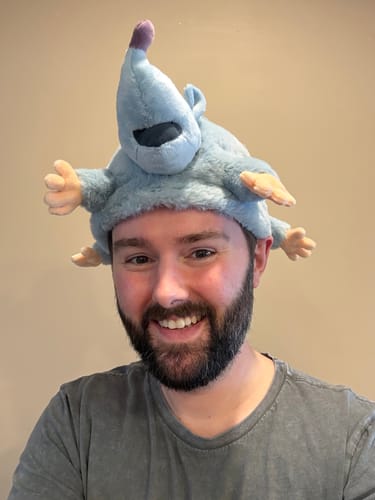 Reviewer smiling while wearing the fuzzy blue Lester's Possum Pal plush hat.