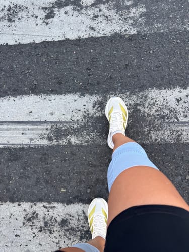 Customer's first-person view of their white Adizero Boston 13 Running Shoes on a paved crosswalk.