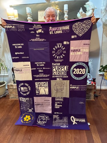 Reviewer holding up a large, purple Project Repat T-Shirt Quilt made from 'PurpleStride' event shirts.