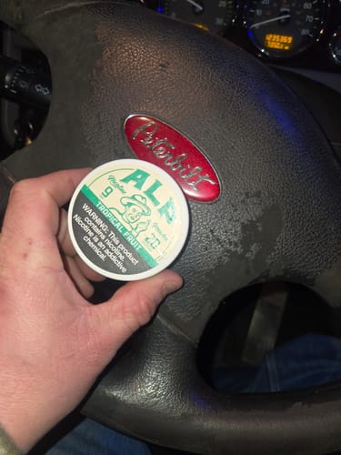 Customer holding a can of Tropical Fruit Nicotine Pouches at the steering wheel of a Peterbilt truck.