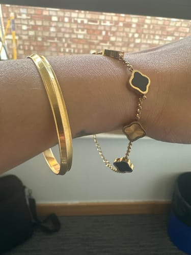 Reviewer's wrist wearing the gold Celine Clover Bracelet with black clovers, styled next to a simple gold bangle.