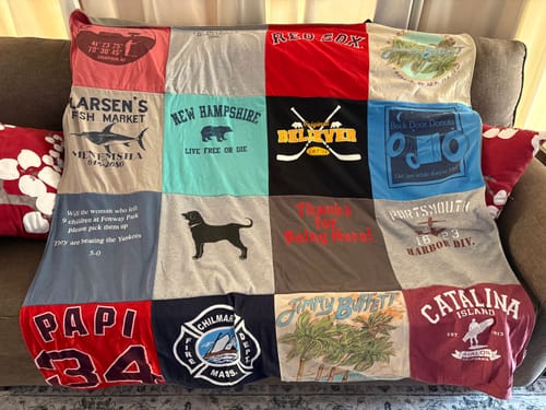 A reviewer's custom Premium T Shirt Quilt, made from a variety of colorful t-shirts, displayed on a sofa.