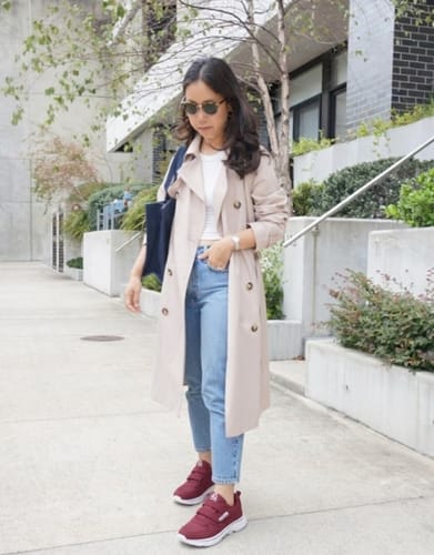 Reviewer standing outdoors in maroon CareStep shoes, paired with jeans and a trench coat.