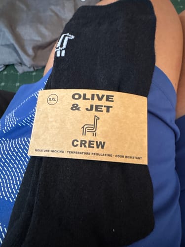 Customer holding a pair of new black Crew Socks in their original cardboard packaging.