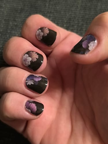 Kundenhand mit aufgetragenen „Midnight Foliage“ UV-Gel-Nagelfolien, die ein florales Muster auf schwarzem Grund zeigen.