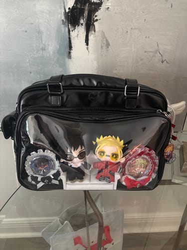 Reviewer's black Coko Stage Bag on a glass table, with plush dolls and decorative pins displayed in the clear front window.