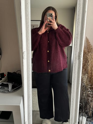 Kundin macht ein Spiegelfoto und trägt den weinroten Bouclé Oversized Cardigan zu einer schwarzen Hose.