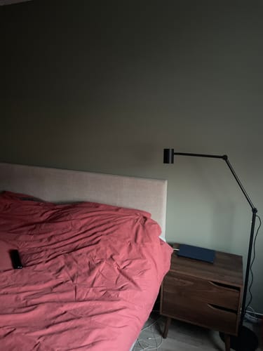 Een recensent toont het nachtkastje van walnoot gebeitst hout, dat naast een bed met een roze dekbed staat.