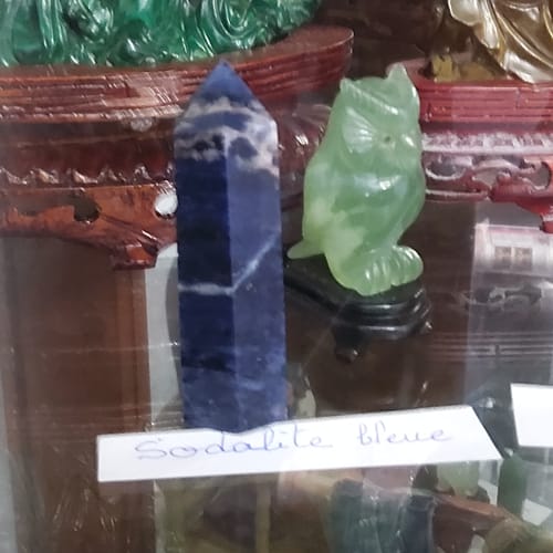 La pointe en Sodalite d'un client, un obélisque bleu avec des veines blanches, posé sur une étagère en verre.