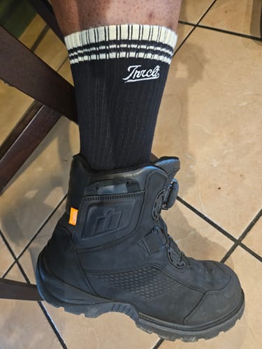 Customer wearing black Script Crew Socks with a white striped cuff inside a black riding boot.