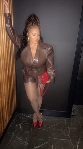 Customer posing in the brown Vegan Leather Trench Romper, styled with pantyhose and red shoes.