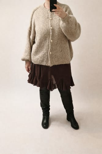 Kundin trägt den beigen, oversized CozyGlam Cardigan zu einem Rock und Stiefeln.