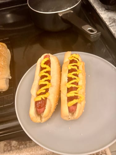 Customer's two Halal Beef Franks served in buns on a plate with yellow mustard on top.