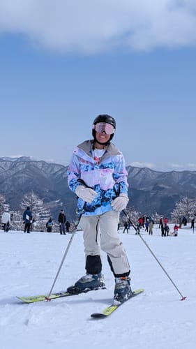 Reviewer skiing on a snowy mountain in the colorful Snow Mountain Classic Versatile Removable Hood Snow Jacket.