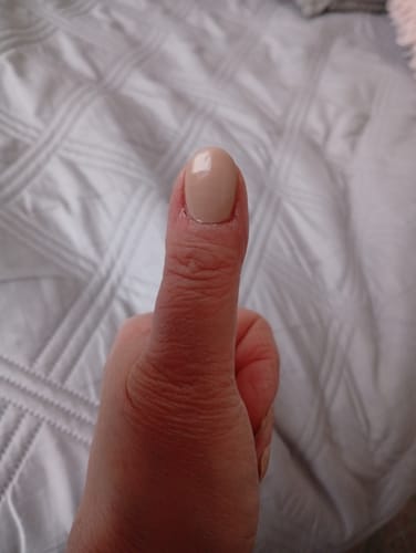 Kunde zeigt die glänzende, nude-farbene UV-Gel-Nagelfolie 'Toasted Almonds' auf einem Daumen.