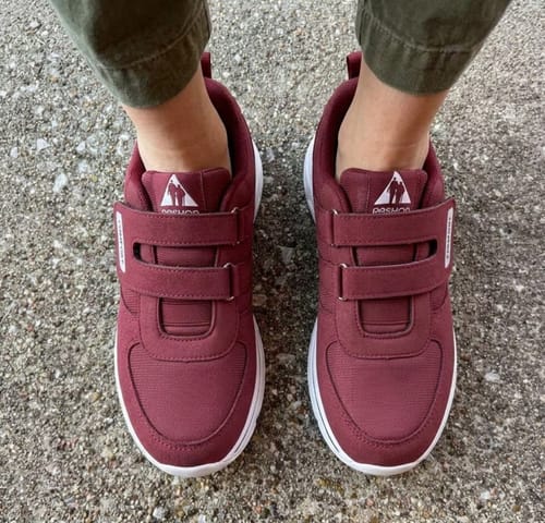 Reviewer wearing a pair of burgundy CareStep shoes with two velcro straps, standing on pavement.