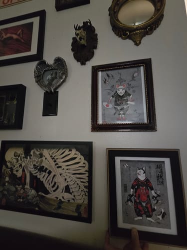 Customer holds the framed Oni Cat Print against a wall with other similar pieces of artwork.