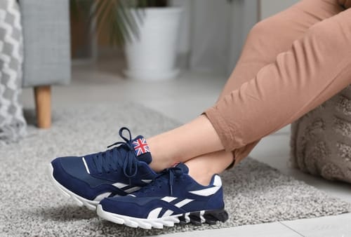 A customer wearing the navy blue Ortho Step 2.0 sneakers with white soles while sitting on a rug indoors.