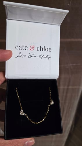 Customer displaying the dainty Irene Heart Station Necklace with shiny crystal hearts in its white gift box.