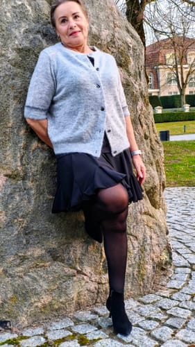 Kundin trägt den schwarzen Rock „Summer“ mit Volantsaum im Freien, kombiniert mit einer Strickjacke.