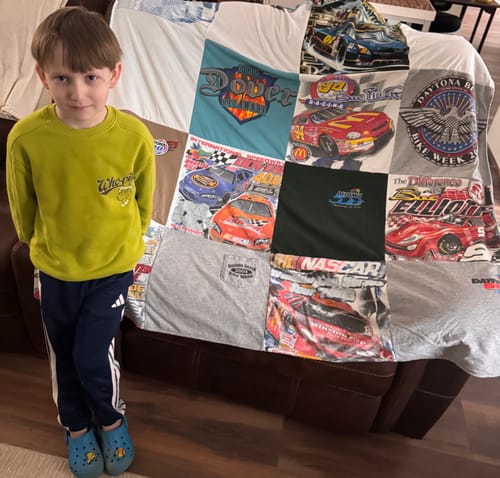 Customer's Premium T Shirt Quilt with a racing theme draped over a brown couch, with a young boy standing beside it.