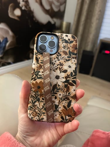 Customer holding a phone with the Lillian case, which has a floral pattern in neutral colors and a matching strap.