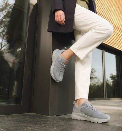 Reviewer posing outdoors in the gray Wide Fit shoes with white pants against a wall.
