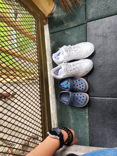 Customer's white Nike P-6000 SE shoes placed on a dark tiled floor next to a second pair of shoes.