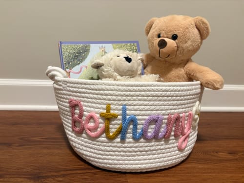 Customer's white knitted basket personalized with 'Bethany' in multicolor yarn, filled with teddy bears and a book.