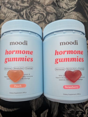 Customer shows two bottles of moodi hormone gummies, Peach and Strawberry, with a matching heart-shaped gummy for each.
