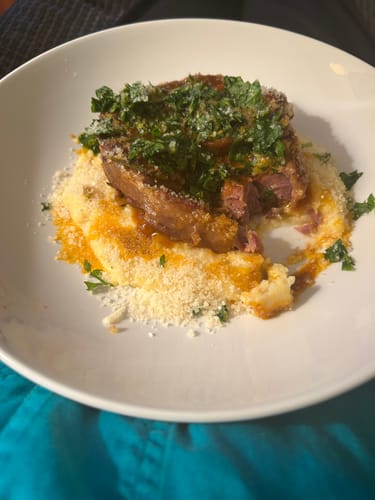 Reviewer's plated Osso buco made from tender Halal Veal Shank Cross-Cut, served over polenta with fresh herbs.