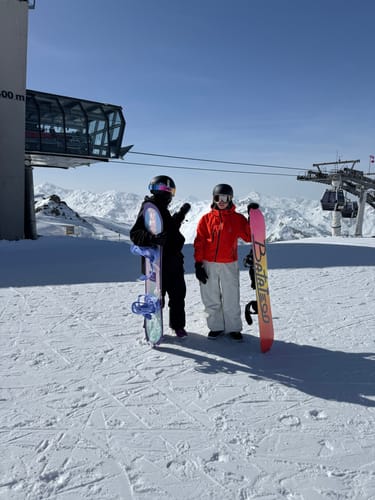 Reviewer standing on a snowy mountain in baggy waterproof snow pants, holding a snowboard.