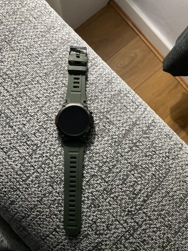 Customer's Gard Pro Ultra 2+ watch with its green strap resting on a textured gray couch arm.